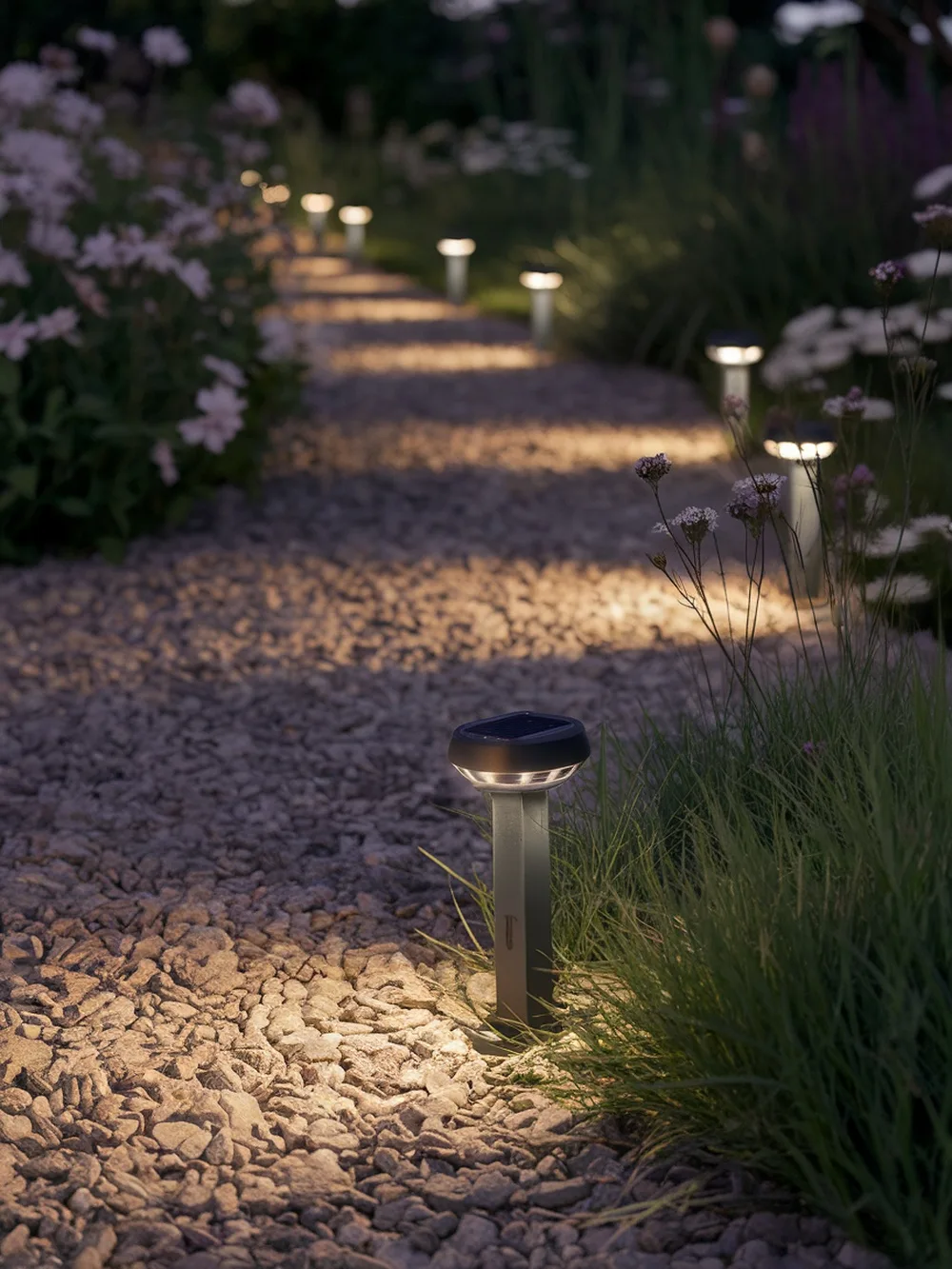 Pathway lights illuminating a garden walkway with flowers and grass.