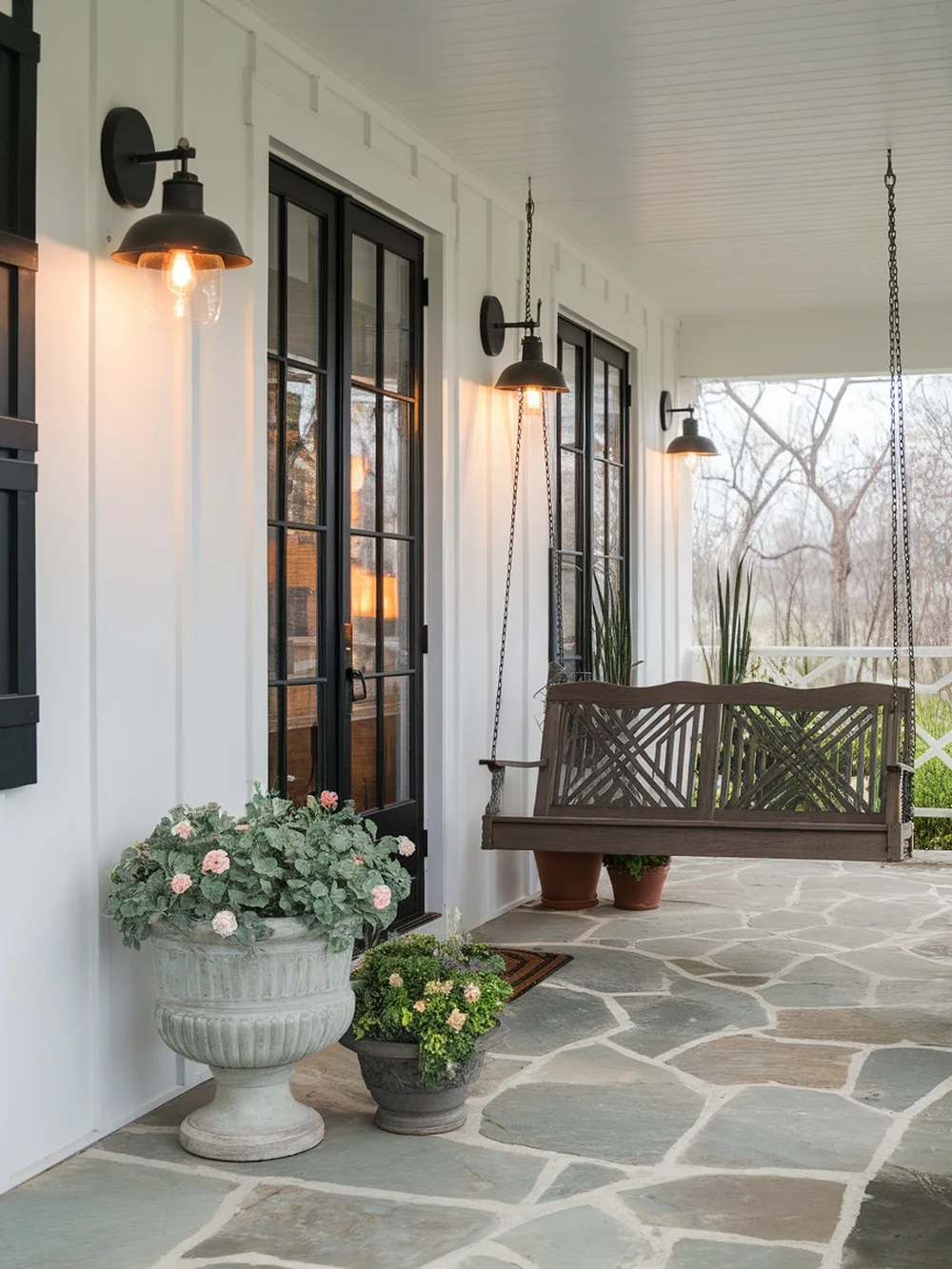A porch with wall-mounted sconces, a swing, and potted plants.